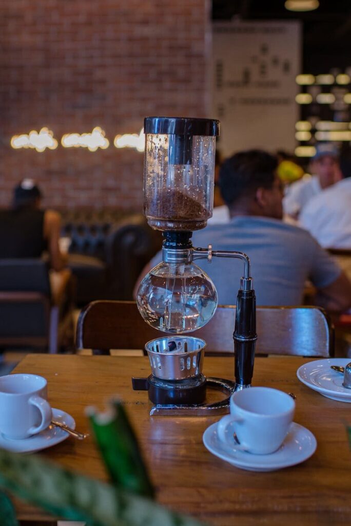 A siphon coffee maker on a café table with cups, creating a cozy atmosphere.
